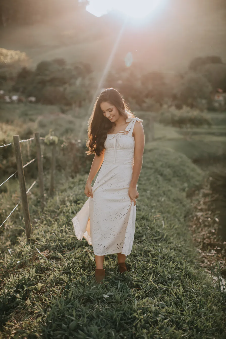 Jovem de vestido branco caminhando no campo ao pôr do sol